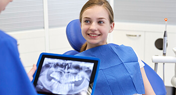 Young girl smiles at dentist holding digital x-rays