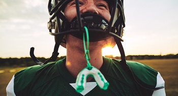 A teenage boy playing football with his sportsguard hanging from his helmet